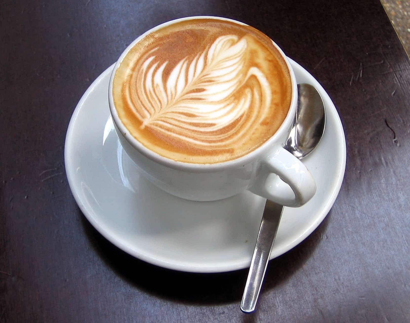 A cup of coffee with a leaf design on top, featuring a flat white or latte.