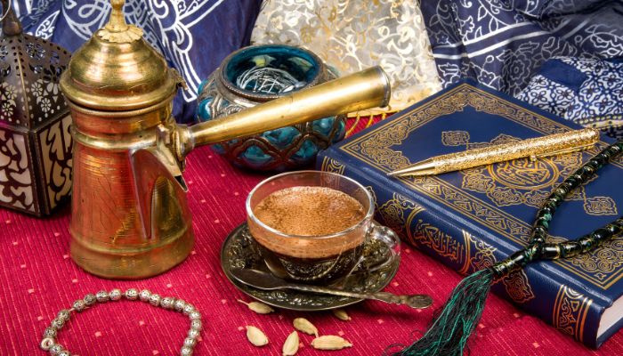Traditional Arabic coffee with cardamom seeds in a glass cup with a brass coffee pot.