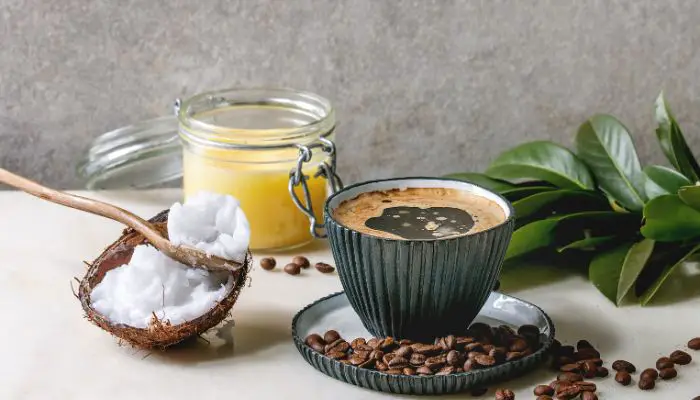 A cup of butter coffee with coconut oil on a saucer with coffee beans scattered around.