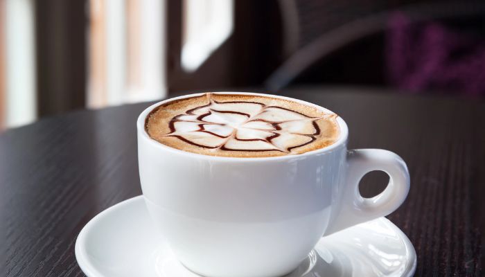 A cup of mocha with artistic latte art on a saucer, set on a dark wooden table.