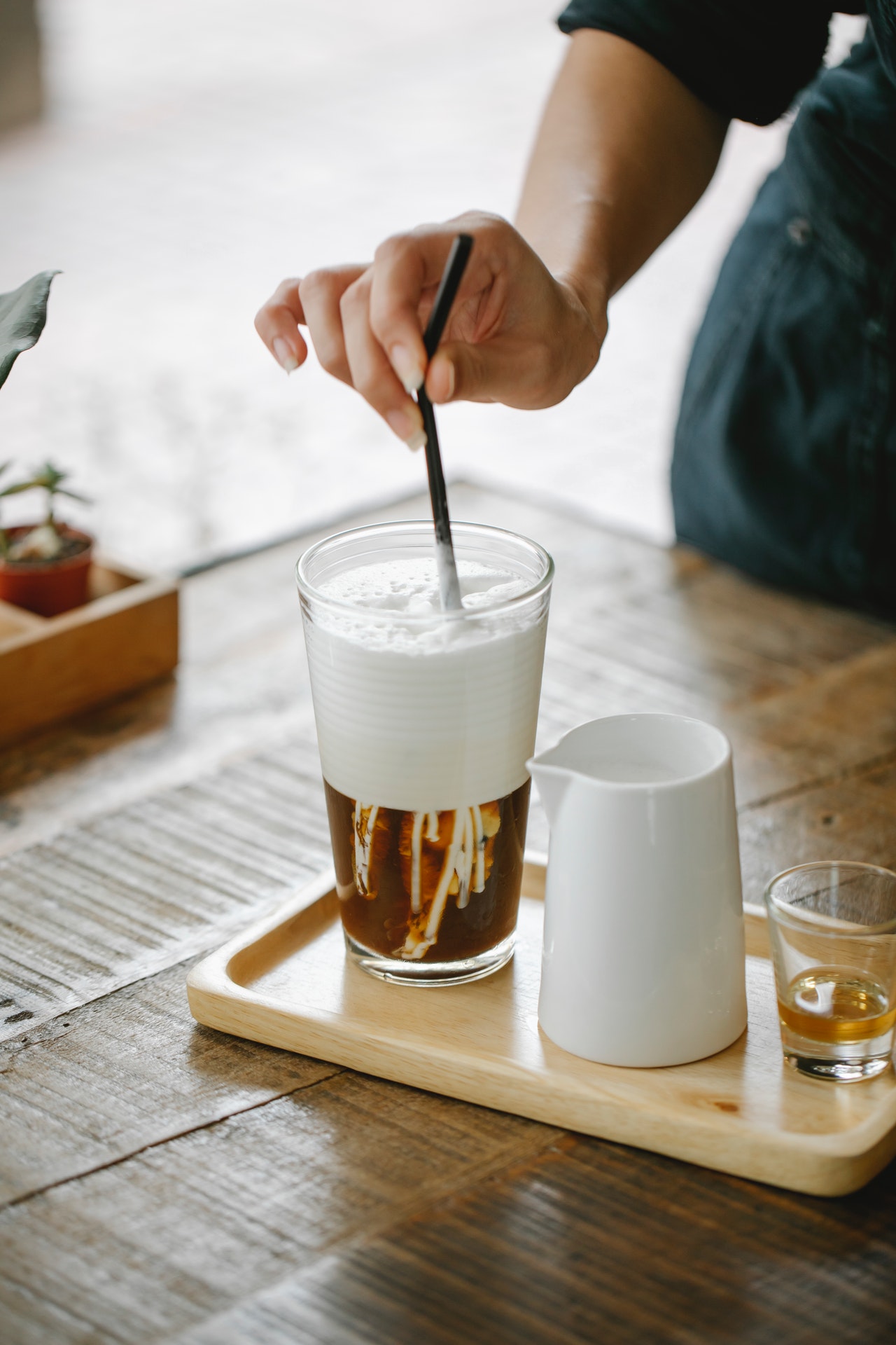 A tray with a glass of cold brew with milk in it, a milk decanter, and an empty shot glass.