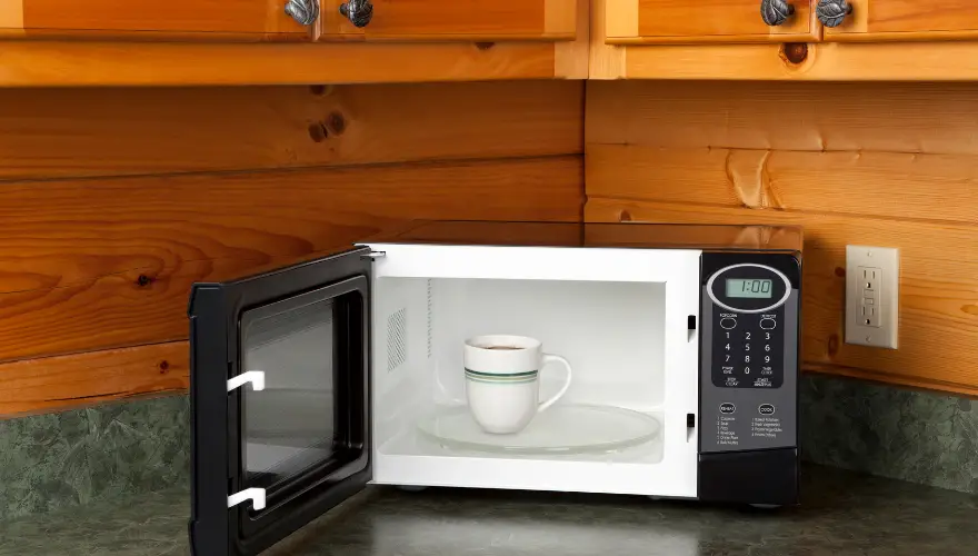 A microwave in a kitchen with a cup of coffee.