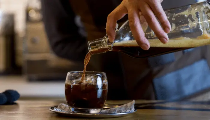 A barista skillfully pouring refreshing coffee into a glass.