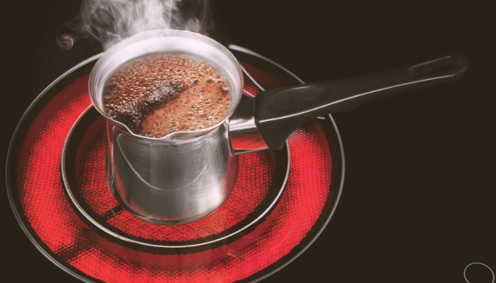 A metal pot filled with cold brew coffee on a glowing red electric stovetop burner.