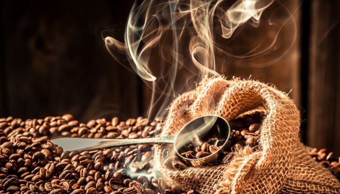 A burlap sack brimming with flavor coffee beans, a metal scoop partially filled, with visible steam or aroma rising from the beans.