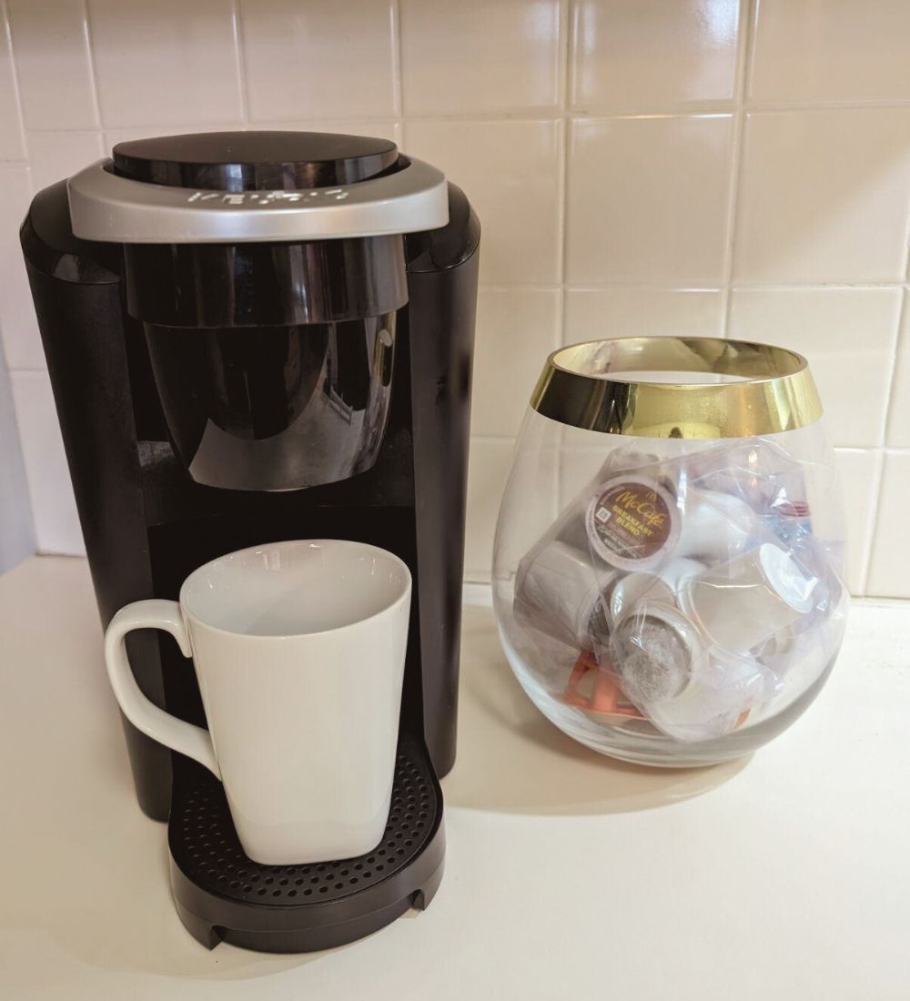 Keurig coffee maker with white cup and container of coffee pods