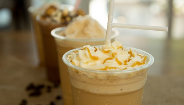 Caramel Frappuccino topped with whipped cream and caramel drizzle, with other similar coffee drinks blurred in the background.